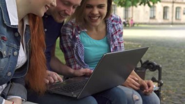 Üç genç öğrenci, iki çekici kız tarafından çevrelenmiş yakışıklı beyaz bir adam, güneşli bir kampüs bankında dizüstü bilgisayarla hevesle meşgul oluyor. Odaklanmış ifadeleri ve günlük kıyafetleri takım çalışmasının ve dışarıda öğrenmenin canlı atmosferini yansıtıyor.