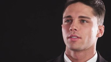 Özel dikim takım elbiseli şık bir genç adam düşünceli bir şekilde dalgın dalgın uzaklığa bakar. Aniden, kameraya döndü, parlak siyah bir arka plana karşı kendine güvenen büyüleyici bir gülümsemeye büründü.