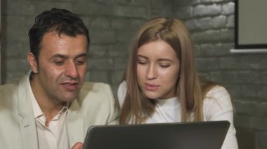 Şık bir ofis ortamında, olgun bir işadamı ve odaklanmış genç bir iş kadını bir dizüstü bilgisayar üzerinde çalışırken dinamik bir tartışmaya girişirler. İşbirlikleri pozitiflik ve takım çalışması yayıyor, deneyim sinerjisini ve yeni fikirleri gözler önüne seriyor.