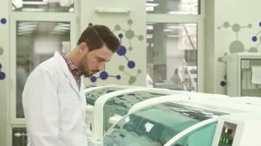 Beyaz önlüklü odaklanmış genç bir adam santrifüj operasyonunu inceliyor ve bilimsel keşfe olan bağlılığını gösteriyor. Ciddi ifadesi bu klinik ortamda hassasiyetin önemini yansıtıyor.