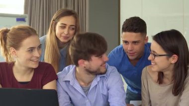 Genç profesyonellerden oluşan canlı bir grup, üç kadın ve iki erkek, şık bir ofiste dizüstü bilgisayarın etrafında toplanırken hevesle başparmaklarını kaldırıyorlar. Parlak gülüşleri ve gevşek tavırları olumlu bir takım ruhunu yansıtıyor.