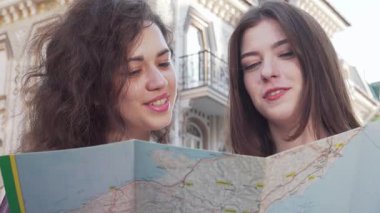 Kırpılmış bir çekim, biri kıvırcık saçlı, diğeri düz saçlı iki genç kadını yakalar, dikkatle büyüleyici bir şehir zeminine karşı bir harita üzerinde çalışırlar. İfadeleri heyecan ve merak yayar. Macera ruhunu somutlaştırır.