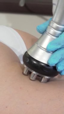 Kendini işine adamış bir güzellik uzmanı, kadın müşterinin kalçasının üzerinde zarif bir RF kaldırma cihazı kullanarak cilt dokusunu geliştirir ve genç bir ışıltıyı teşvik eder. Bu yenilikçi anti-selülit tedavisi şık bir güzellik kliniğinde son teknoloji ile birleştirildi.