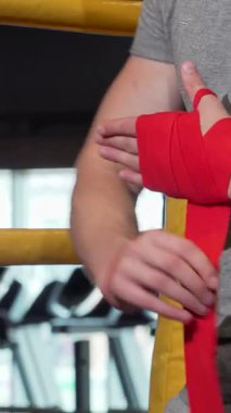 Dinamik yakın plan çekimde kararlı bir erkek boksör cesur kırmızı bilek bandajlarını ustalıkla sarıp spor salonunda heyecan verici bir egzersiz için hazırlanıyor. Bu görüntü, sporcuların sarsılmaz bağlılıklarının altını çizerek özgüven ve azim yayar.