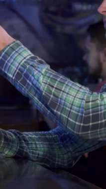 Kahverengi saçlı, şık, genç, beyaz bir adam buzlu birasından tatmin edici bir yudum alıyor. Yan profili rahatlatıcı. Samimi bar atmosferi, ahşap aksanlar ve sıcak aydınlatmalarla süslenmiş, bu mükemmel arkadaşlığı davet ediyor.