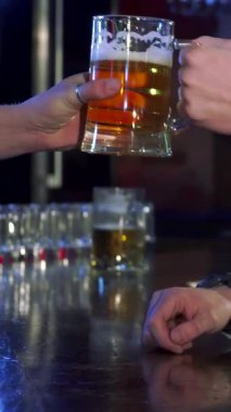 Kahverengi saçlı şık, beyaz bir adam barda soğuk bir bira içiyor. Yumuşak bar ışıklarının ışıltısıyla aydınlanan rahat yan profili. Kırsal ahşap tezgah ve canlı atmosfer bu an için mükemmel bir zemin oluşturur.