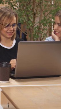 Neşeli sarışın bir kız, parlak ve modern bir çalışma alanında iş arkadaşlarının parlak laptopuna bakması için hevesle el kol hareketi yapıyor. Yakınlarda, şık kahverengi saçlı bir kadın notlar alırken yakışıklı bir adam kitap okuyor ve canlı bir atmosfer yaratıyor.