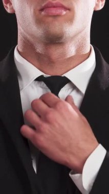 Çarpıcı bir genç adam kravatını titiz bir özenle, göz alıcı bir cazibeyle ve entelektüellikle parlak bir siyah zemine göre ayarlar. Kendine güveni ve geniş gülümsemesi çekici özelliklerini artırarak modern zarafetin çekici bir portresini oluşturuyor.