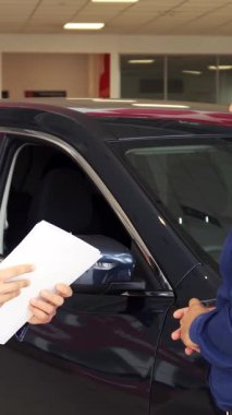 Modern bir araba galerisinde, şık giyimli bir satıcı ve memnun bir alıcı güven dolu bir tokalaşmayı paylaşıyor ve başarılı bir anlaşma imzalıyor. Pürüzsüz araç arka planda parıldıyor. Bu önemli anın heyecanı ve profesyonelliğini yansıtıyor.