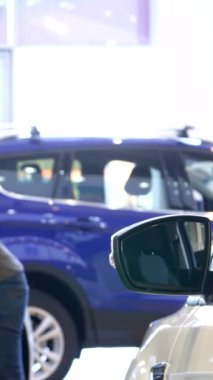 Tarz sahibi bir siyahi adam keskin bir ilgiyle öne eğiliyor, galerideki modern bir arabanın parıldayan yüzeyini inceliyor, yansıması camda parıldıyor. Bu genç, sakallı Afrikalı Amerikalı müşteri heyecan ve merak yayıyor.