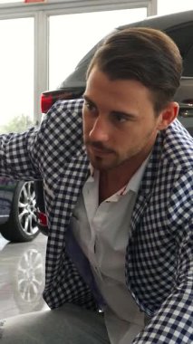 Koyu renk saçlı, bakımlı sakallı şık bir adam ışıldayan yeni arabasının yanında diz çöküp, ışıldayan bir gülümsemeyle baş parmağını kaldırıyor. Modaya uygun bir ceket ve kot pantolon giyerek, aydınlık, modern gösteri salonunda neşe ve güven saçar,