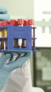 Koruyucu gözlüklü ve mavi lateks eldivenli odaklanmış genç bir laboratuvar asistanı, çeşitli örneklerle dolu renkli test tüplerini titizlikle inceliyor. Yoğun konsantrasyonu ve hassasiyete olan bağlılığı hayati önem taşıyan şeyleri aydınlatıyor.