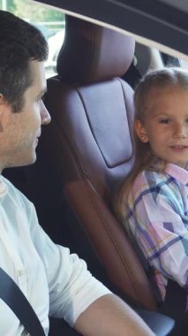 Zengin kahverengi deri koltuklarla süslenmiş şık bir arabada, koyu saçlı genç bir baba renkli bir ekose gömlek giyen kızıyla neşeli bir sohbet ediyor. Karşılıklı şakalaşmaları sıcaklık ve sevgi yayar, aşkın özünü yakalar