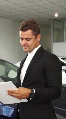 Modern bir araba galerisinde, iki şık giyimli adam arabaların özellikleriyle ilgili ayrıntılı belgeleri inceleyerek derin bir tartışmaya girişiyor. Şatafatlı seçenekleri keşfederken ve gösteriş yaparken canlı atmosfer heyecanla doludur.