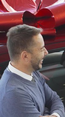 Canlı bir araba galerisinde, neşeli bir alıcı ve şık bir satıcı neşeli bir yayla süslenmiş göz kamaştırıcı kırmızı bir arabanın yanında sözleşme detaylarını incelerken neşeli bir sohbeti paylaşıyor. Sivri gri takım elbiseli satıcı...