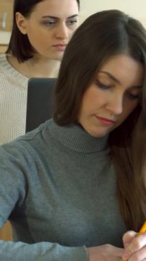 Parlak ve modern bir konferans salonunda, odaklanmış genç Kafkas öğrencileri çalışma kitaplarına özenle notlar yazıyorlar. Sade gri kazaklı şık bir esmer kız ve arka planda düşünceli sınıf arkadaşı, her ikisi de akranlarıyla çevrili.