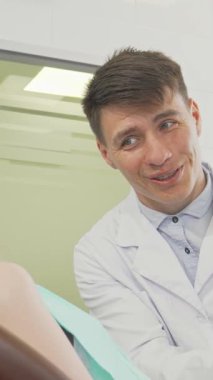 Göz kamaştırıcı genç bir kız diş muayenesi sırasında kameraya göz kamaştırıcı bir gülümseme sergiliyor, saf neşe saçıyor. Detaylı bir diş modelini gururla sergileyen arkadaş canlısı erkek dişçi, parlak klinikte sıcak ve davetkar bir atmosferi teşvik ederek diş hekimliği yapıyor.