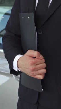Özel dikim siyah takım elbiseli dengeli bir satış müdürü gururla sunar çarpıcı gri bir sedanın yanında bir araba anahtarı, profesyonellik ve başarı yayar. Dinamik alçak açılı çekim hareketli bir bayiliğin canlı atmosferini yakalıyor,