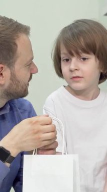 Memnun bir baba ve büyüleyici genç oğlu eczanede beyaz bir alışveriş torbasını hevesle keşfederken büyüleyici bir anı paylaşıyorlar. Renkli sağlık ürünleriyle dolu canlı raflarla çevrili neşeli bağlantıları sıcaklık ve sıcaklık yayıyor.