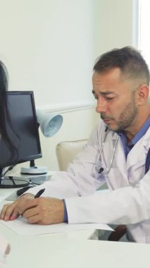 Parlak, modern bir muayenehanede, şefkatli bir doktor genç bir kadınla temas kurar, röntgeni dikkatle inceler. Huzurlu atmosfer, sağlık ve tedavi hakkındaki önemli konuşmaları yönetirken güven ve ilgiyi vurgular.