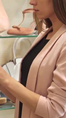 Uzun, dalgalı saçlı şık bir genç kadın şık bir bej ayakkabıyı şık bir butikte inceliyor, stil ve sofistike bir şekilde. Moda aksesuarları ve ayakkabıları ile çevrelenmiş, modern perakendenin özünü somutlaştırıyor.