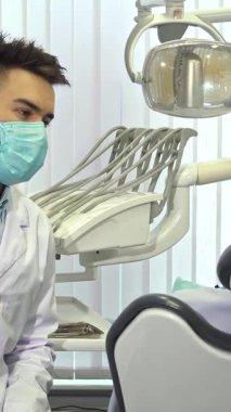 Beyaz önlük ve koruyucu giysiler içinde odaklanmış genç bir beyaz dişçi, şık ve çağdaş bir diş muayenehanesinde müşterinin dişlerini titizlikle inceliyor. Parlak, steril çevre, yetenekli insanlar olarak profesyonellik ve bakım duygusunu geliştirir.