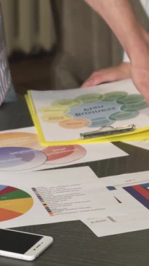 Bu dinamik yakın çekim, stratejik bir toplantı sırasında canlı diyagramları analiz etmekle uğraşan iş profesyonellerini sergiliyor. Eller coşkuyla renkli grafikleri ve grafikleri gösterirken, atmosfer işbirliğiyle uğulduyor.