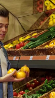 Sarışın, modaya uygun, beyaz bir adam hareketli bir hipermarketten titizlikle olgun domatesleri ve parlak dolmalık biberleri topluyor. Bu canlı sahne, alışveriş arabasını renkli bir dizi ile doldururken sağlıklı bir yaşamın neşesini yayıyor.