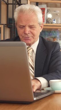 Şık bir kafede, iki iş ortağı sıkı bir tokalaşma içine girer, güven ve işbirliği yayar. Genç adam, şık bir sakalı var, kendinden emin bir şekilde yaşlı meslektaşının yanında oturuyor, o da elinde bir kalemle panoya işaret ediyor,