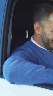 Zevkli bir adam, yeni arabasının heyecanını kucaklarken zevkle ışıldar. Elini gösterişli direksiyona nazikçe yaslar. Gururlu gülüşü ve şık gri süveteri bir başarı ve lüks anını yansıtıyor.