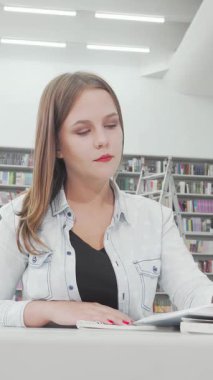 Büyüleyici düşük açılı bir çekim kendini adamış genç bir kız öğrenciyi modern bir kütüphanede çalışırken kaşı konsantrasyonla yarılmıştı. Etrafı renkli kitaplarla çevrili ve aydınlık, çevresel aydınlatmalarla çevrili.