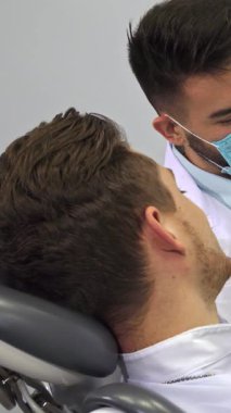 Parlak bir diş kliniğinde, beyaz önlüklü, yetenekli, sakallı bir dişçi ayrıntılı bir model kullanarak insan dişlerinin karmaşık düzenini tutkuyla gözler önüne seriyor. Şık bir saç kesimi olan özenli erkek hasta, anlayışla başını sallar.