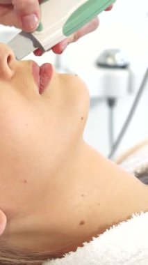 Yetenekli bir kozmetik uzmanı genç beyaz bir kadının kusursuz cildinde ultrasonik bir fırçayla süzülerek doğal güzelliğini huzurlu bir kuaför ortamında artırıyor. Cihazın yumuşak uğultusuyla tamamlanan rahatlatıcı ortam.