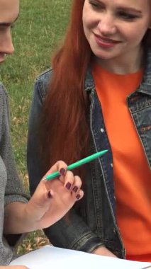 Birinde dalgalı sarı saçlı, diğerinde parlak kırmızı bukleli iki genç kadın, çalışmalarına sade ahşap bir bankta dalmış durumdalar. Bereketli yeşilliklerle çevrili ve sıcak güneş tarafından öpülmüş, odaklanmış ifadeleri güzel bir bağın yansımasını yansıtıyor