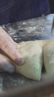 Kendini işine adamış bir fırıncı, elleri un tozuyla kaplı, parlayan tezgahta hamuru ustalıkla kesiyor, hareketli bir mutfağın enerjisiyle çevrili. Bu büyüleyici sahne, pişirmenin sanatsal ve tutkusunu vurguluyor.