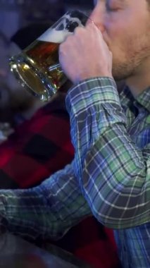 Yakışıklı, kahverengi saçlı bir adam, kahkaha ve gevezelikle dolu bir barda soğuk bira bardağını kaldırırken neşe saçıyor. Şık bir damalı gömlek giyen bu çekici beyaz erkek kutlama ruhunu ve dostluğu somutlaştırıyor.