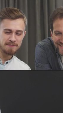 Şık sakallı yakışıklı genç bir iş adamı ve olgun erkek arkadaşı parlak siyah bir dizüstü bilgisayardaki verileri incelerken neşeli bir tartışmayla meşguller. Gülüşleri profesyonelliği ve takım çalışmasını yansıtıyor.