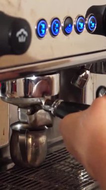 Gösterişli gri tişörtlü kendini adamış genç bir adam cilalanmış espresso makinesinin kolunu ustalıkla çeker ve zengin, aromatik bir kahve çeker. Makinenin canlı düğmeleri ve pırıl pırıl metali büyüleyici bir zemin oluşturur.