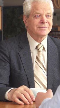 Sıcak ışıkla dolu büyüleyici bir kafede, iki Kafkasyalı iş ortağı buluşmalarını sonlandırıyor, dostluk ve profesyonellik yayıyorlar. Yaşlı, gri saçlı bir adam, doğmakta olan meslektaşıyla tokalaşırken zevkten dört köşe olur.