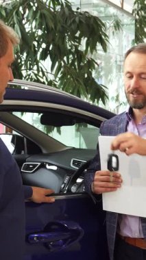 Gösterişli, modern bir araba galerisinde, ışınlama satıcısı hem neşe hem de memnuniyet saçan yeni sahibine anahtarları teslim eder. Canlı sergi salonu, yemyeşil ve şık araçlarla süslenmiş, bu kutlama için mükemmel bir zemin hazırlıyor.