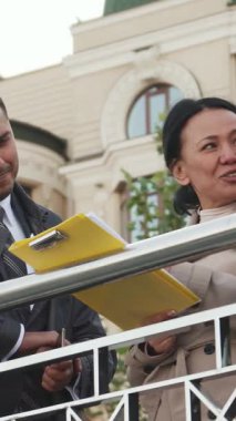Canlı bir şehir parkında, takım elbiseli bir erkek parlak sarı bir klasördeki bir belgeye hevesle işaret ederken, genç bir kadın dikkatle dinlerken, başka bir erkek onların animasyon tartışmalarına katkıda bulunuyor. Yeşillik ve modern mimari ile çevrili.