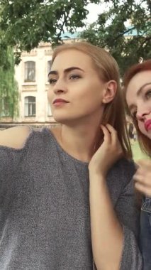 İki genç kadın, biri canlı kızıl saçlı, diğeri de göz kamaştırıcı bir sarışın, üniversitelerinin yakınındaki güneşten sırılsıklam olmuş bir parkta selfie çekiyorlar. Bereketli yeşilliklerle ve benekli güneş ışığıyla çevrelenmiş kahkahaları havayı dolduruyor,