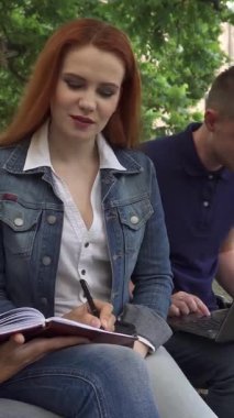 Kendini işine adamış kahverengi saçlı bir öğrenci defterine tutkuyla yazarken, kot giyen meraklı bir kızıl saçlı sınıf arkadaşlarının notlarından büyüleniyor. Yakınlarda, yakışıklı, beyaz bir erkek dizüstü bilgisayarının başında canlı bir atmosfer yaratıyor.