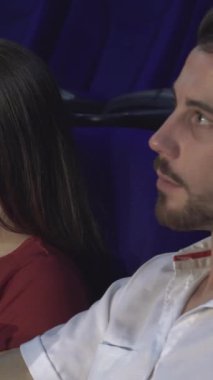 Heyecanla dolu canlı bir sinemada iki çift, büyüleyici sinema dünyasına dalmış bir şekilde yan yana otururlar. Kırmızı gömlekli kız sevinçle ışıldarken ekranın sıcacık parıltısı onların gülüşlerini ve keyifli anlarını yansıtıyor.