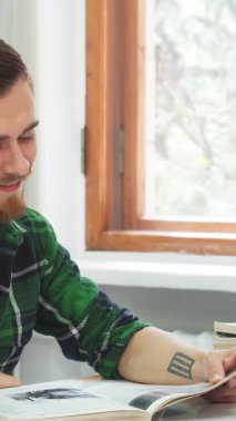 Siyah saçlı ve şık sakallı neşeli bir genç adam kitabındaki komik bir pasajdan büyülenerek kahkahalara boğuluyor. Güneş ışığı pencereden içeri doluyor, gülümseyen yüzüne sıcak bir parıltı saçıyor, rahat ve davetkar bir atmosfer yaratıyor.