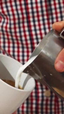 Şık, kareli gömlekli yetenekli genç bir adam kapuçinonun üstünde nefis bir kalp tasarımı yaparak beyaz bir fincana titizlikle süt döker. Bu büyüleyici an, latte sanatının özünü yansıtıyor. Tutkunun yetenekle buluştuğu an.