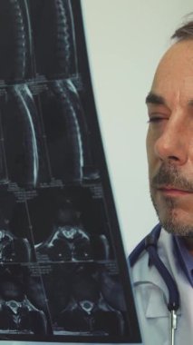 Kendini adamış beyaz önlük ve steteskop giymiş genç bir erkek terapist, sıcak bir gülümseme ve özen göstererek röntgen filmini inceliyor. Onun parlak ofis ayarları güven ve uzmanlık atmosferini geliştirir, hastaları davet eder