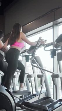 Dinamik bir dikiz aynası, geniş pencerelerden süzülen doğal ışığın sıcaklığıyla aydınlatılan eliptik spor ayakkabıları üzerinde enerjik bir şekilde çalışan iki büyük kadını gösteriyor. Paylaştıkları gülücükler ve motive edici enerjileri güç yayıyor.