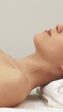 Güzel esmer bir kız, yumuşak beyaz bir havluya sarılı bir masaj masasının üzerinde zarif bir şekilde uzanır. Sıcak gülüşü, huzurlu spa ortamında neşe saçar. Bu çarpıcı beyaz kadın model yüzünü kameraya doğru çeviriyor, dinginliği somutlaştırıyor ve