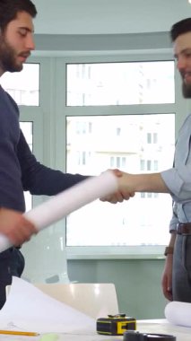 Gösterişli, güneşli bir ofiste iki genç erkek mimar, başarılı bir işbirliğini kutlamak için coşkuyla el sıkışıyor. Tarz sahibi beyaz tasarımcılar, detaylı planlar ve canlı turuncu bir başlık ile çevrili, profesyonellik saçıyor ve...